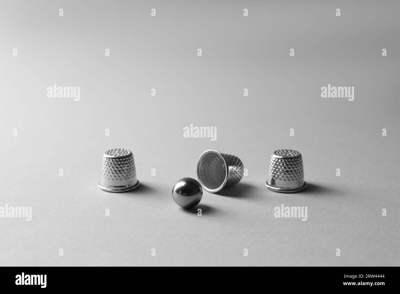 Metal thimbles and ball on light grey background. Thimblerig game Stock ...
