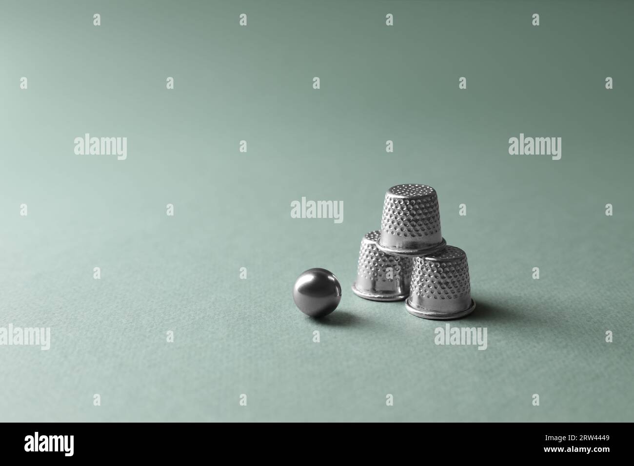 Metal thimbles and ball on pale olive background, space for text ...