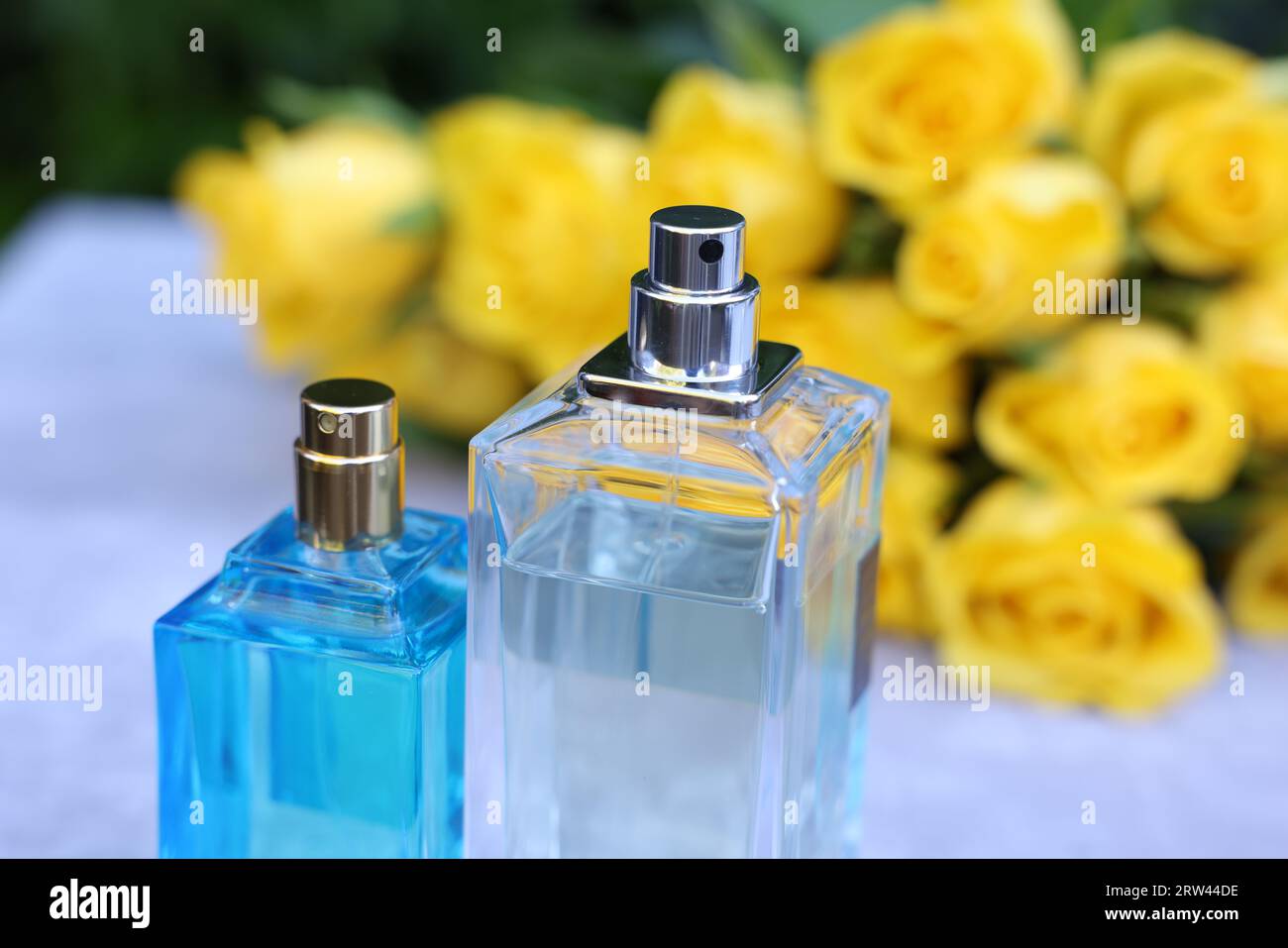 Perfumes and beautiful bouquet of yellow roses on light table, selective focus Stock Photo