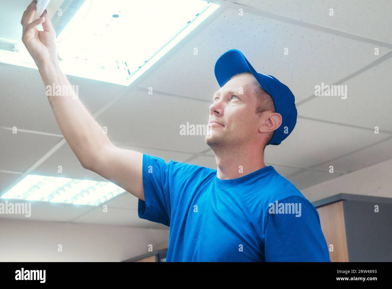 Electrician installs fluorescent lamp in ceiling light in office ...