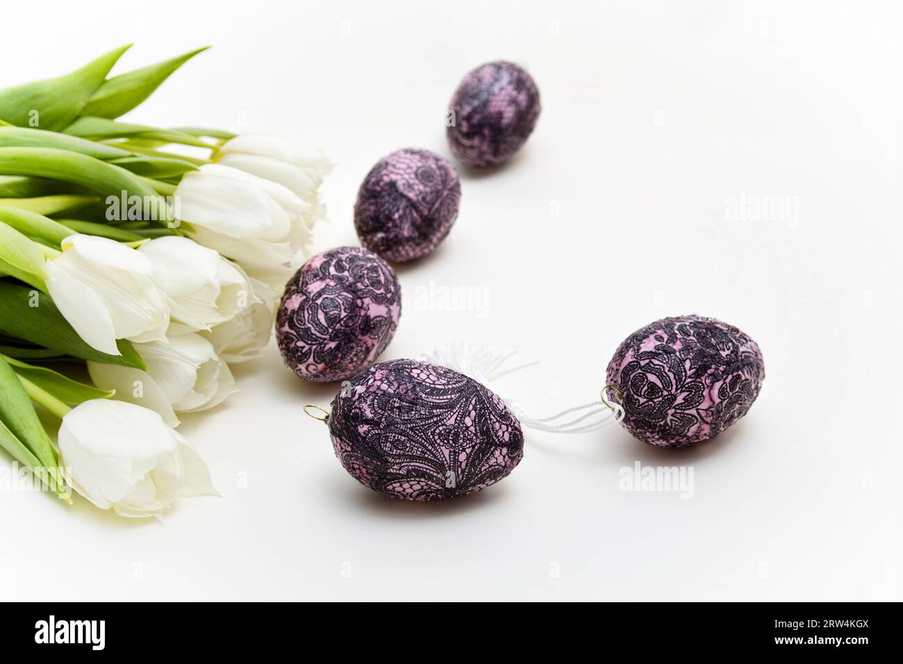 A bouquet of white tulips lies next to decorated Easter eggs on a light ...