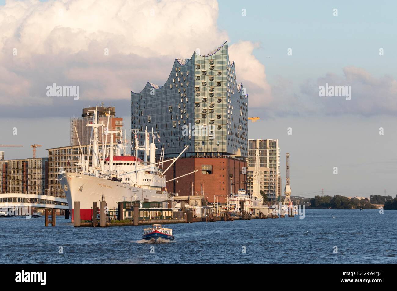 A barge underway on the Elbe, behind it the museum ship Cap San Diego, Ueberseebruecke and Elbe Philharmonic Hall in the evening light in Hamburg Stock Photo