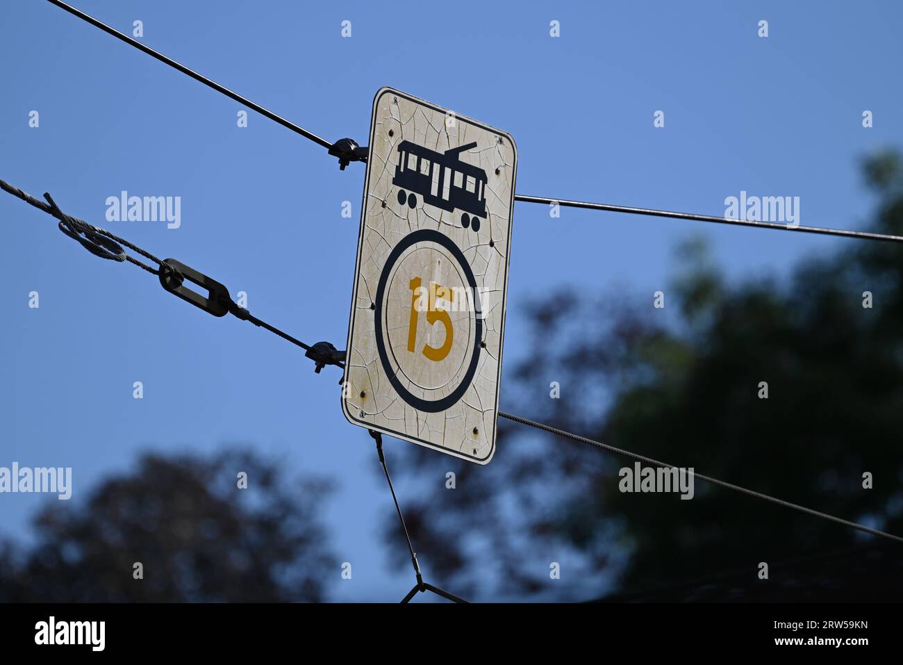 Cracked, weathered, and discoloured tram speed limit sign, featuring the number 15 and an icon of a tram, suspended by wires above a road Stock Photo