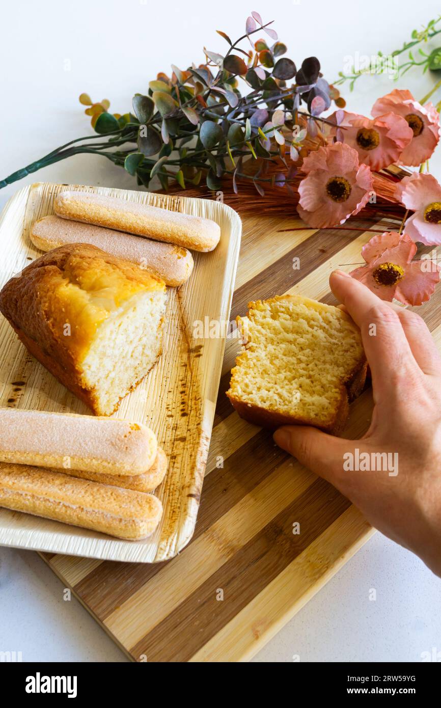 Homemade sponge cake. Woman's hand holding a slice. Decorated table. Vertical shot. Stock Photo