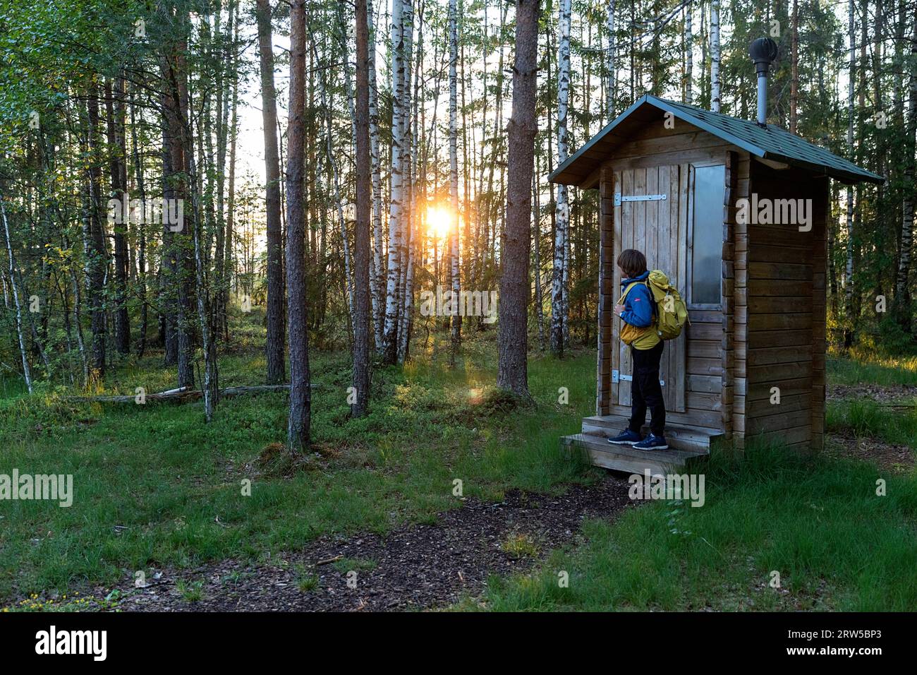 Boy tourist near wooden public toilet on Beautiful forest Mannikjarve hiking trail in lush pine forest in Endla Nature Reserve in Estonia Stock Photo