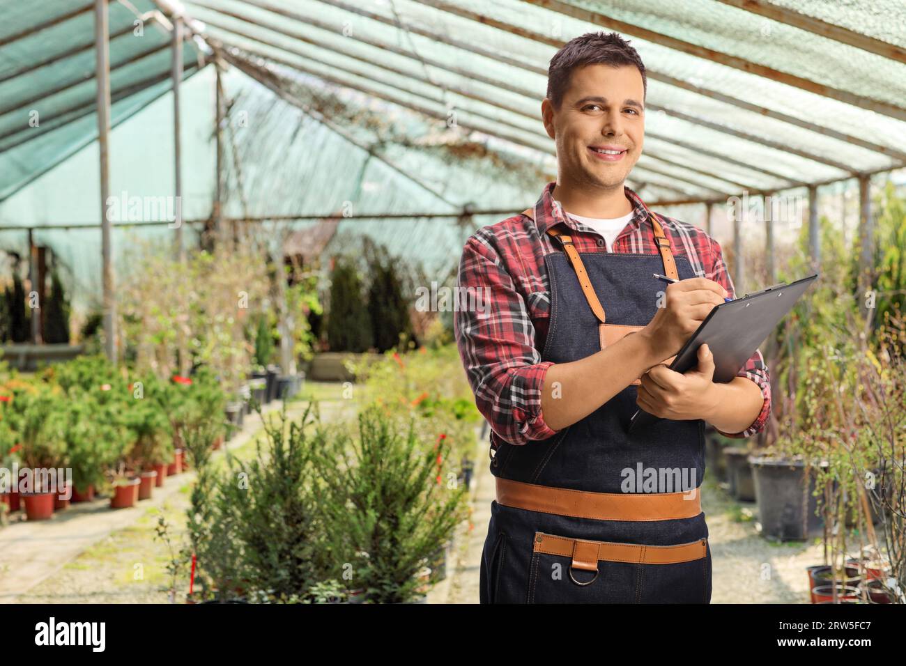 Male florist writing a document and standing inside a greenhouse Stock Photo