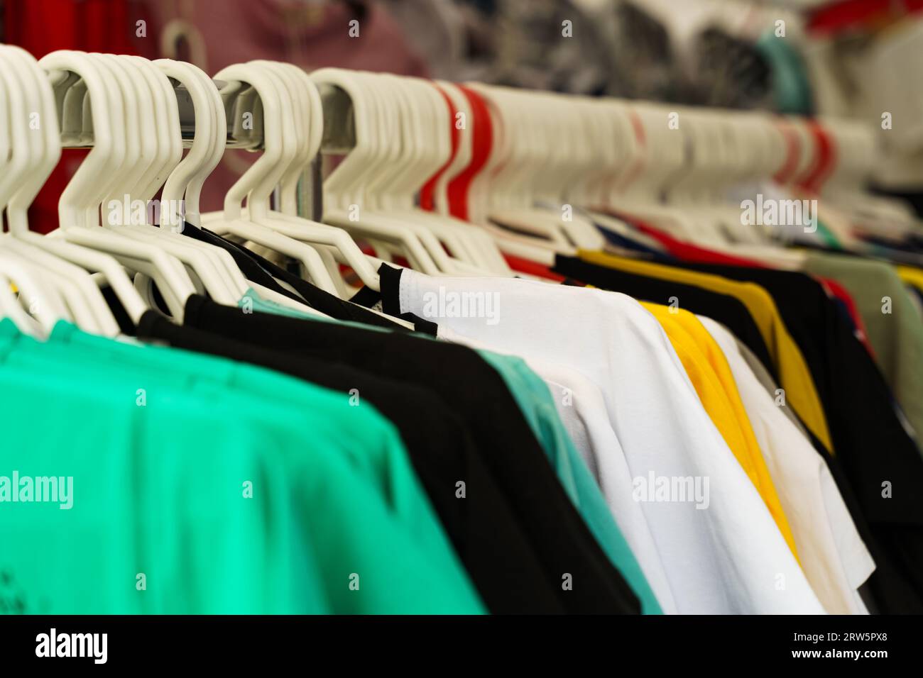 Multi-colored T-shirts hang on hangers on the counter of a trade tent at a fair. Close-up. Stock Photo