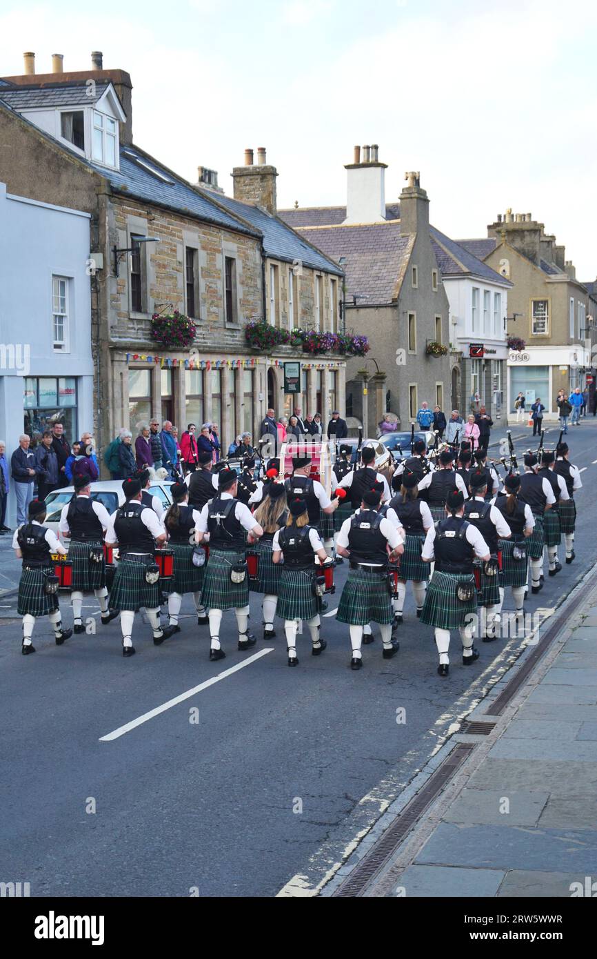 The Kirkwall City Pipe Band marches past historic stone buildings as they perform traditional pipe and drum music in downtown Kirkwall, Orkney Island Stock Photo