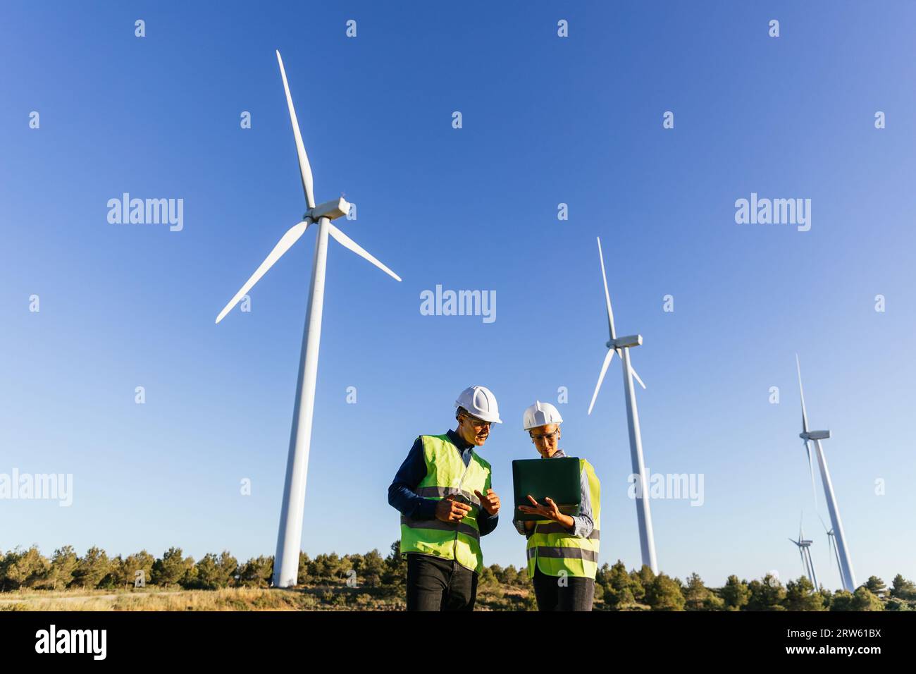 Engineers using laptop while working in wind energy field. Stock Photo