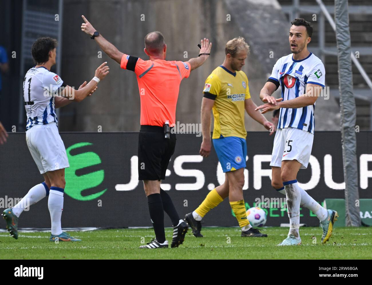 17 September 2023, Berlin: Soccer: 2. Bundesliga, Hertha BSC - Eintracht Braunschweig, Matchday 6, Olympiastadion, Hertha's Fabian Reese (l) and Haris Tabakovic (r) complain to referee Marco Fritz (M) about handball in the Braunschweig penalty area. After video evidence, the referee awards a penalty. Photo: Soeren Stache/dpa - IMPORTANT NOTE: In accordance with the requirements of the DFL Deutsche Fußball Liga and the DFB Deutscher Fußball-Bund, it is prohibited to use or have used photographs taken in the stadium and/or of the match in the form of sequence pictures and/or video-like photo ser Stock Photo