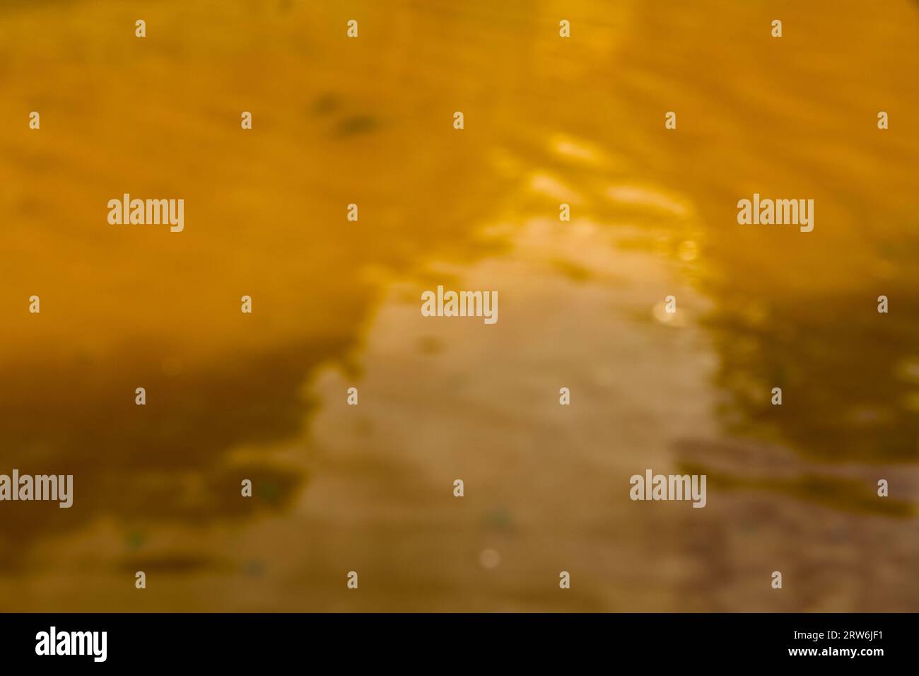 Blurred defocussed view of ripples on orange yellow water. Stock Photo