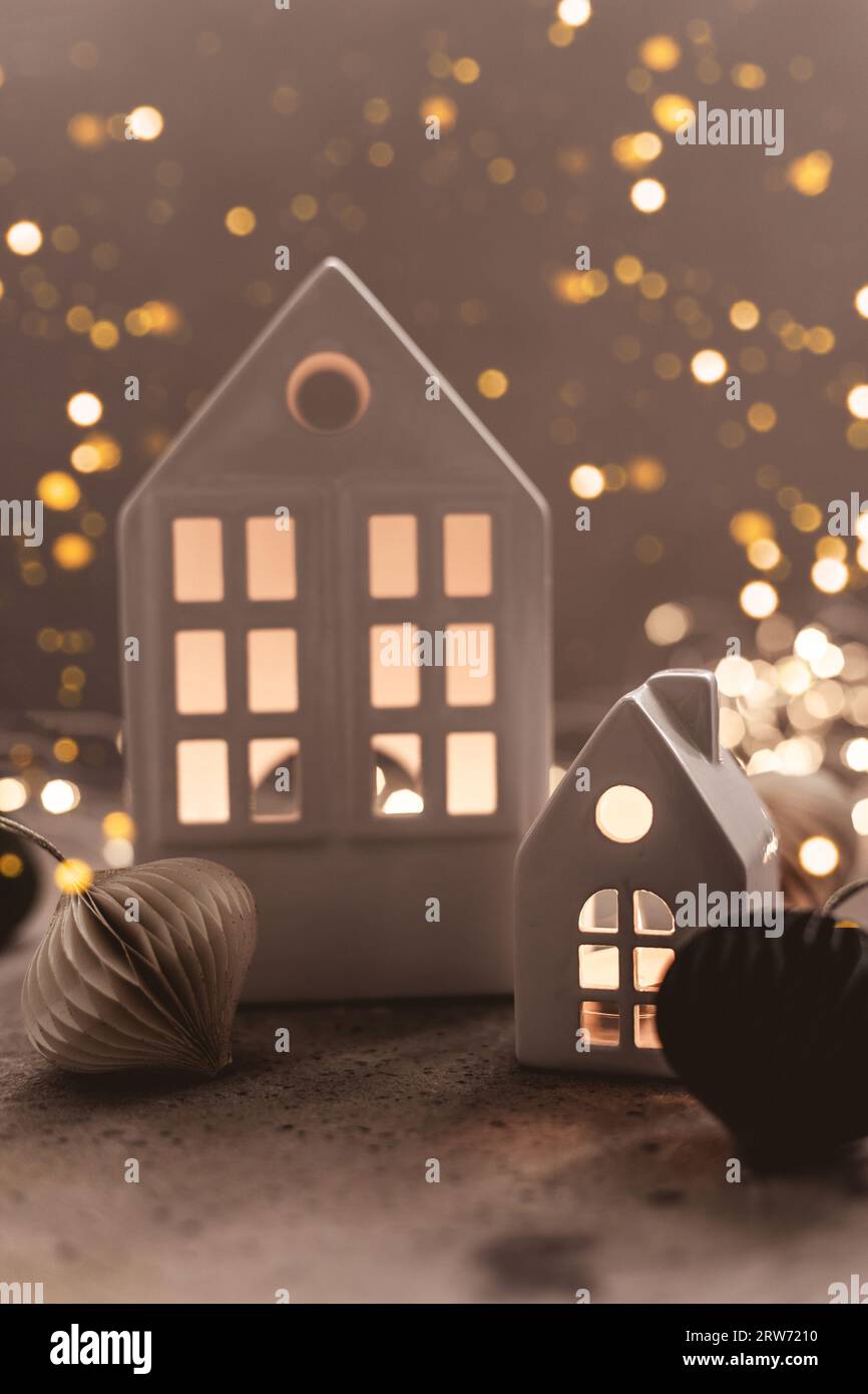 Christmas background with white ceramic house and paper ballon a background. Christmas background with garland lights bokeh. Stock Photo