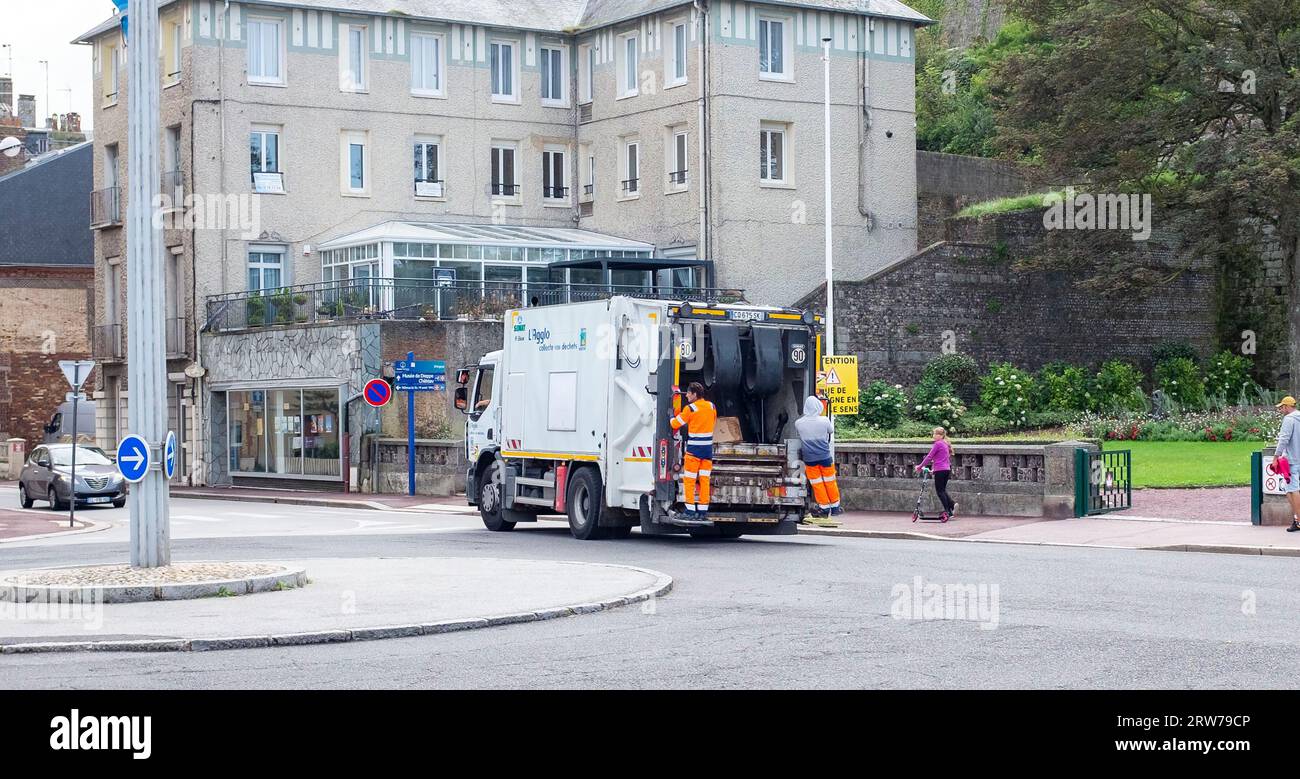 Refuse workers hang off the end of their vehicle in Dieppe , Normandy Stock Photo
