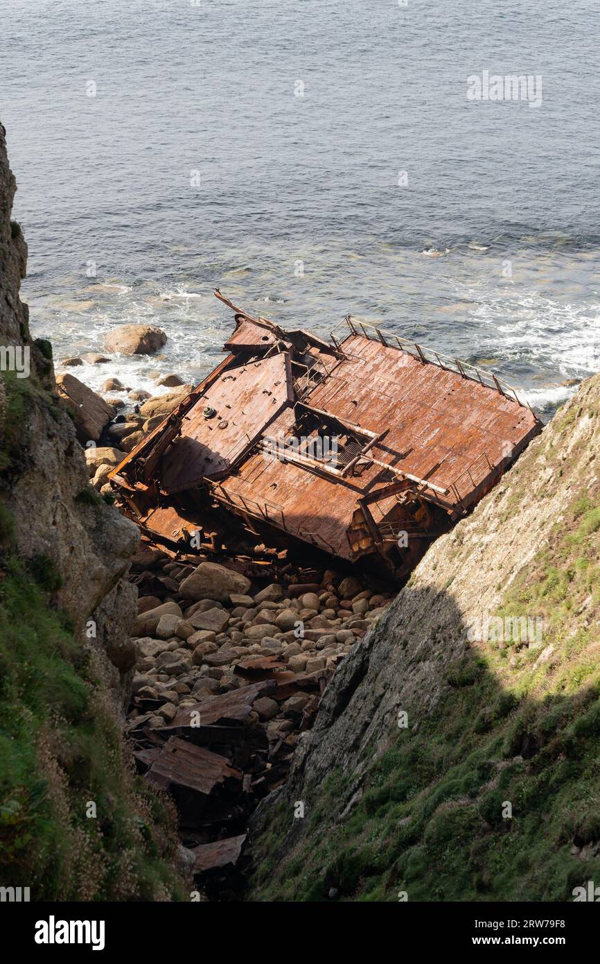 Rusted shipwreck remains on rocky Cornish coastline with waves and ...