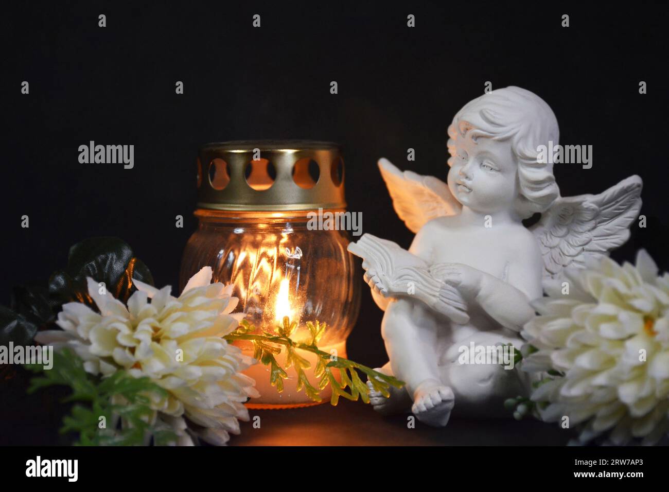 Sympathy card with an angel figurine, votive candle and flowers on black background Stock Photo
