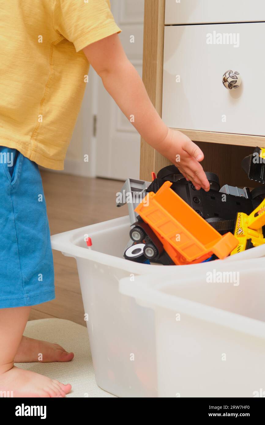 The child is learning about organization by cleaning up his toys. Kid toddler boy aged two years Stock Photo