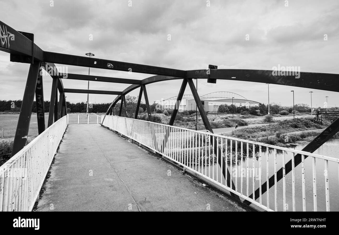A black and white image looking over a footbridge crossing the Leeds Liverpool canal towards the DW Stadium in Wigan seen in September 2023. Stock Photo