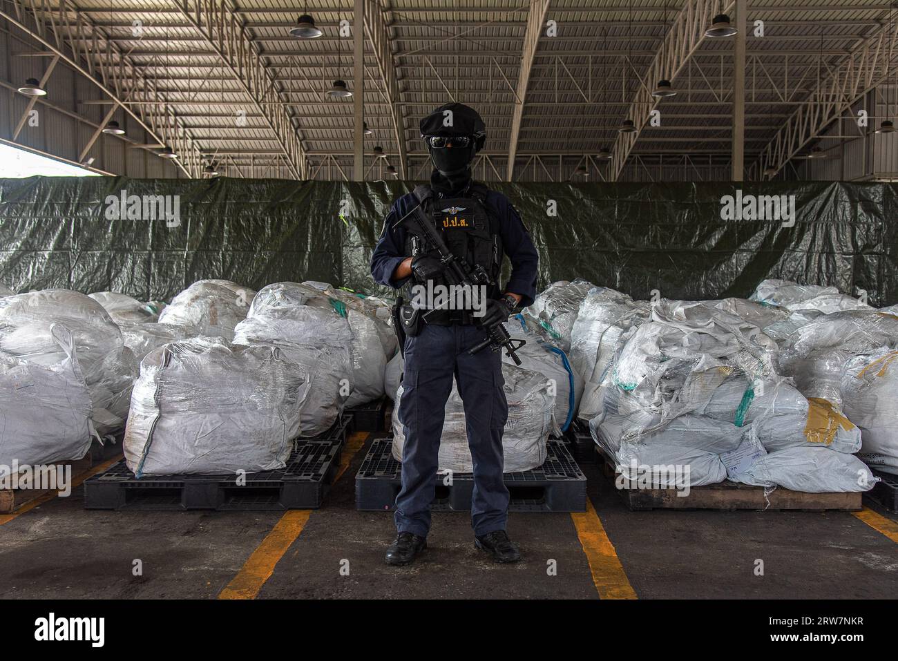 A Thai police special forces officer stands on guard next to the bags of confiscated illegal drugs during the destruction of confiscated narcotics ceremony at a facility in Bang Pu industrial estate, Samut Prakan province in Thailand. Thai authorities destroyed over 25 tons of illegal drugs including Amphetamine, Methamphetamine and Heroin. Thailand government led by Prime Minister Srettha Thavisin announced his government will eliminate the abuse of illegal drugs especially Methamphetamine. (Photo by Peerapon Boonyakiat/SOPA Images/Sipa USA) Stock Photo