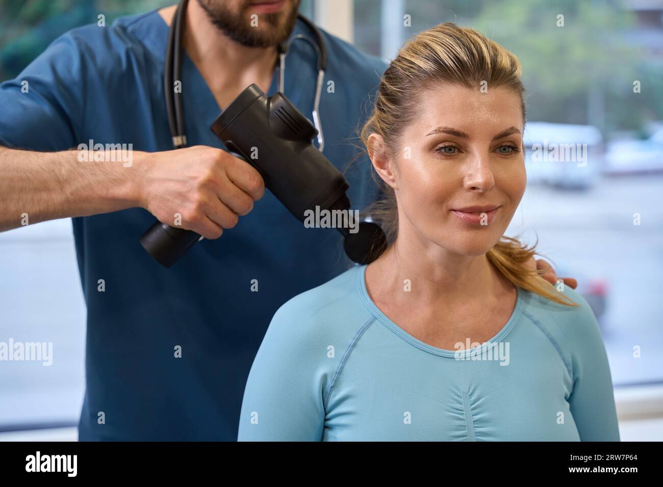 Closeup of physiotherapist using massage gun on female patient