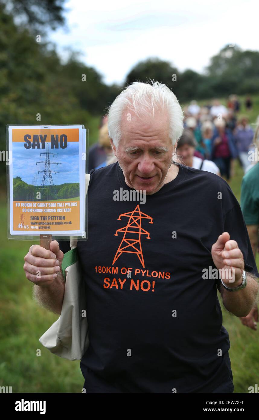A protester wearing a tshirt saying ‘180km of pylons Say No' stands in front of a rural scene