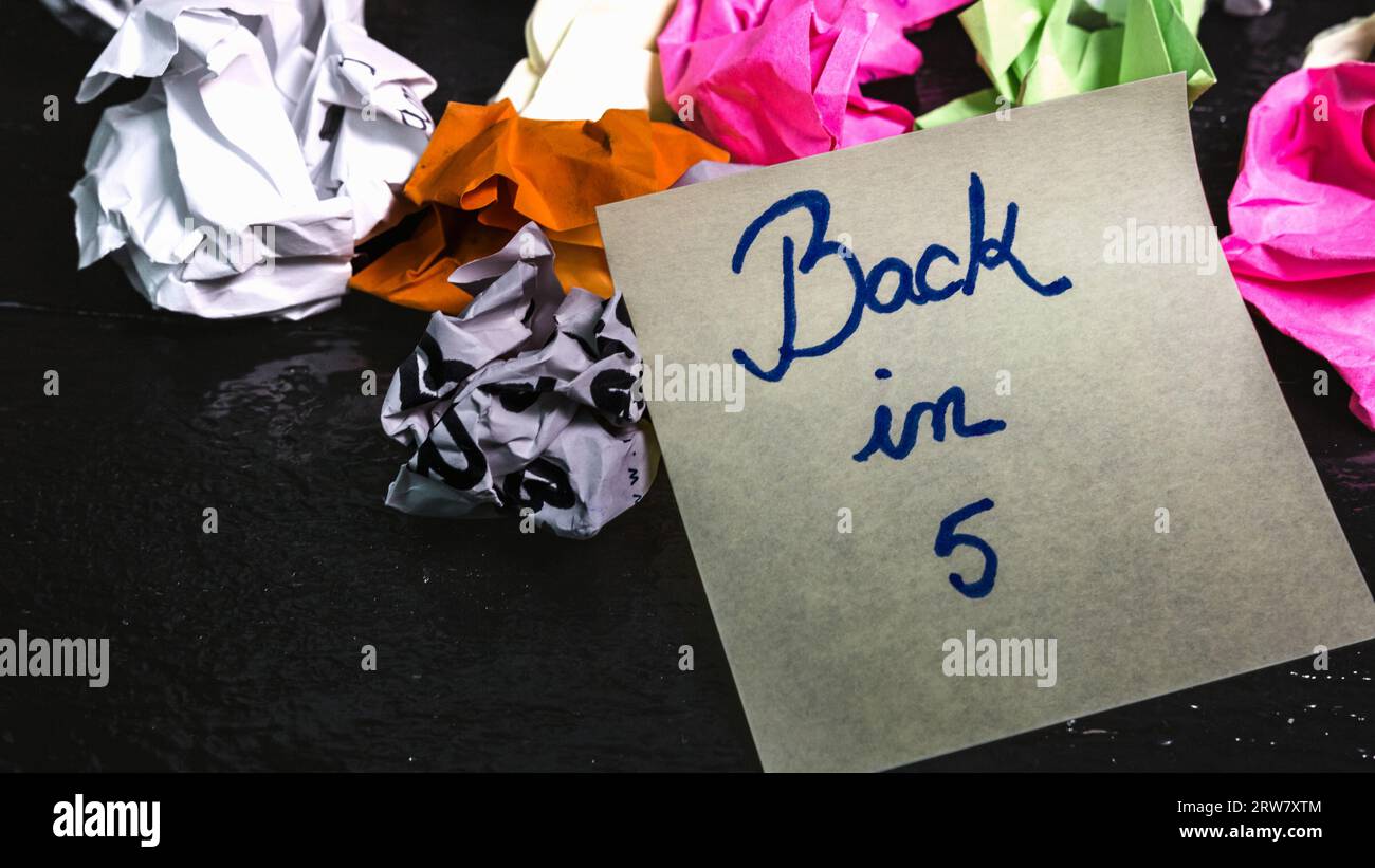 Writing back in 5 on memo post reminder. Text on sticky paper, crumpled ...