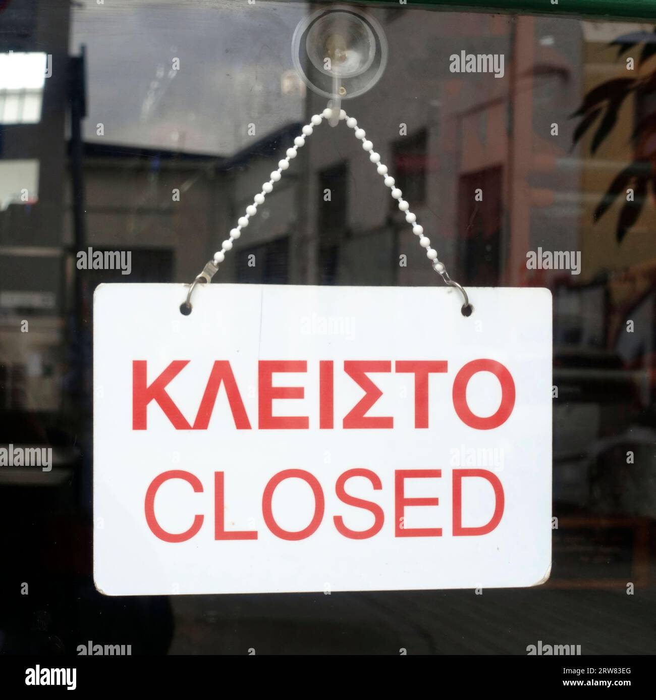 Closed sign in Greek and English languages hanging on the door of a shop in Greece Stock Photo