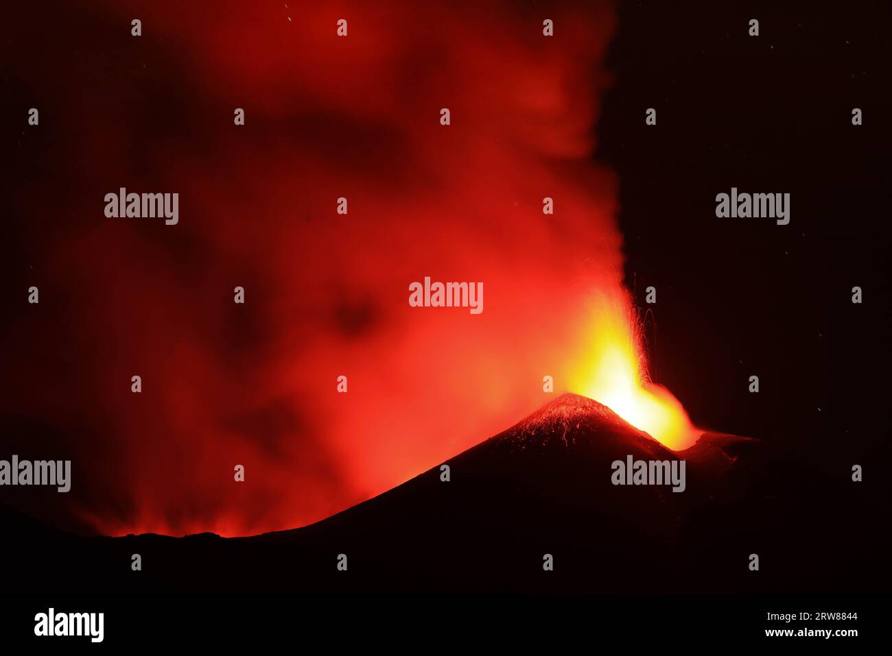 L'Etna in un'eruzione lavica notturna con cratere sagomato in controluce e grandi emissioni di fumo in una vista panoramica del vulcano siciliano Stock Photo