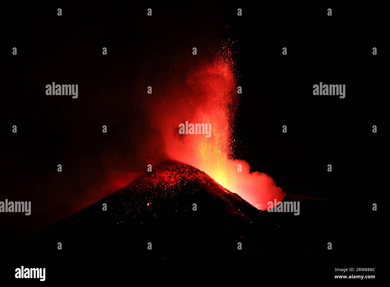 L'Etna in un'eruzione lavica notturna con cratere sagomato in controluce e grandi emissioni di fumo in una vista panoramica del vulcano siciliano Stock Photo