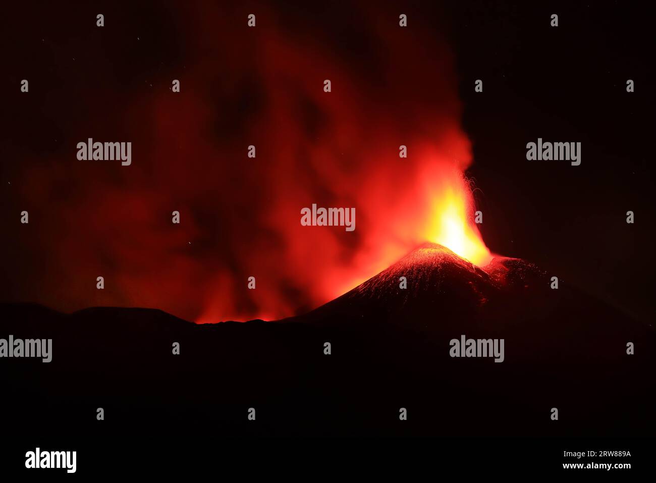 L'Etna in un'eruzione lavica notturna con cratere sagomato in controluce e grandi emissioni di fumo in una vista panoramica del vulcano siciliano Stock Photo