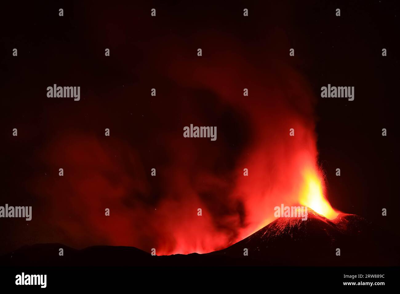 L'Etna in un'eruzione lavica notturna con cratere sagomato in controluce e grandi emissioni di fumo in una vista panoramica del vulcano siciliano Stock Photo