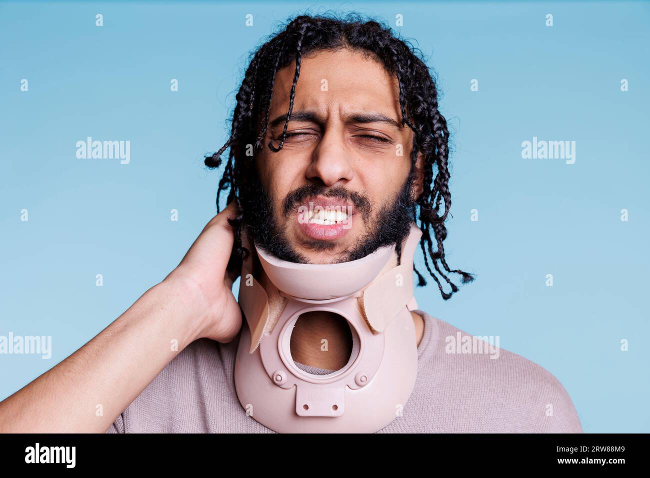 Arab man wearing cervical collar and grimacing in pain while touching