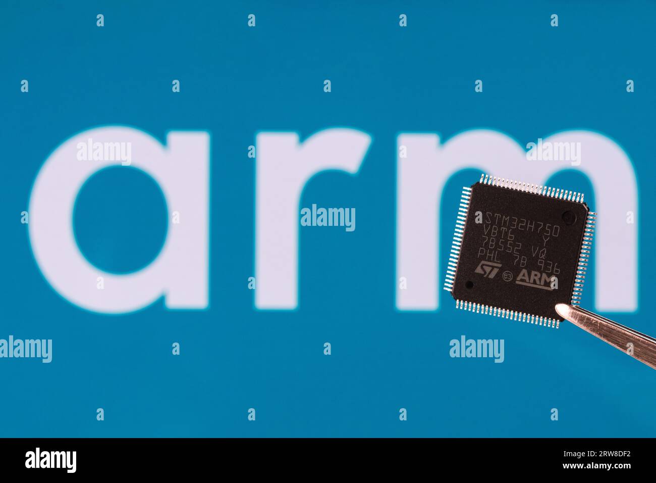 ARM logo seen on STM32 microchip hold in tweezers and blurred ARM company logo on the background. London, United Kingdom, September 17, 2023 Stock Photo