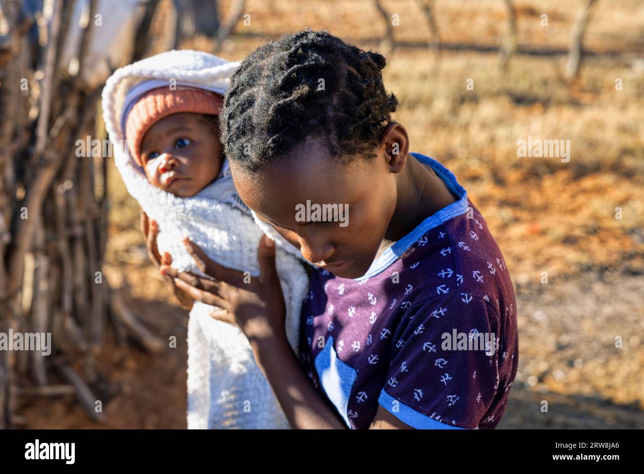 african girl holding a baby, village, backyard view, at sunset, the hardness of  spending teenage years having a small child Stock Photo
