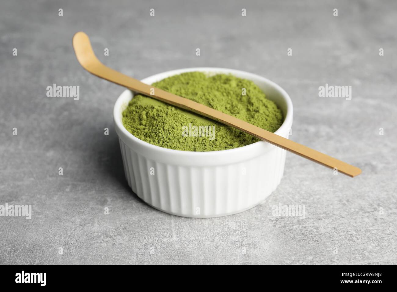 Green matcha powder and bamboo scoop on light grey table, closeup Stock Photo