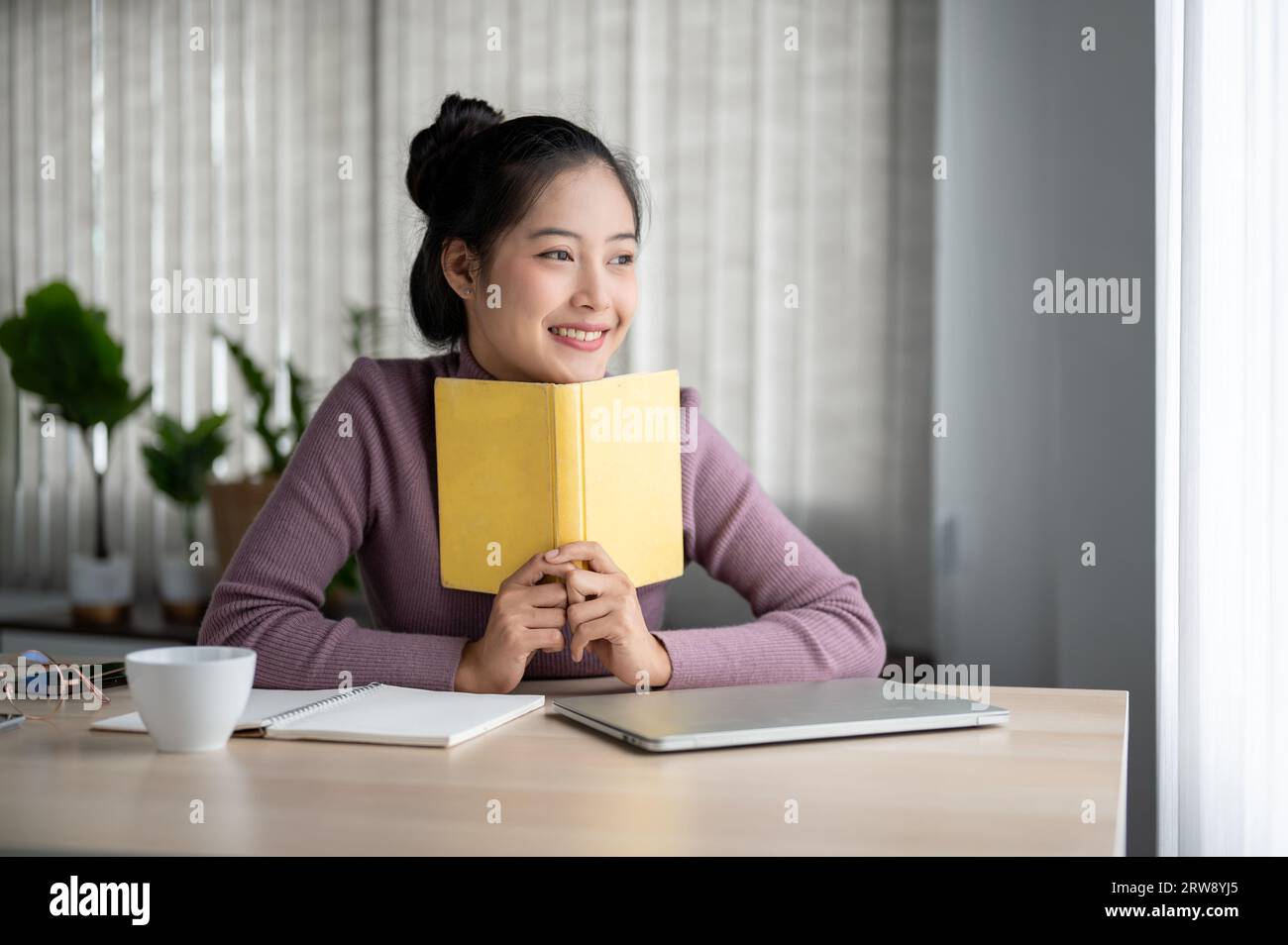 A beautiful and inspired young Asian woman is looking out the window ...