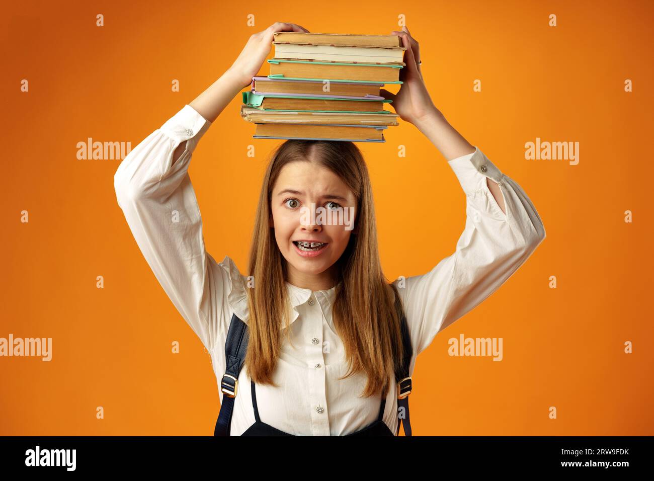 Teen schoolgirl holding stack of books over head on yellow background ...