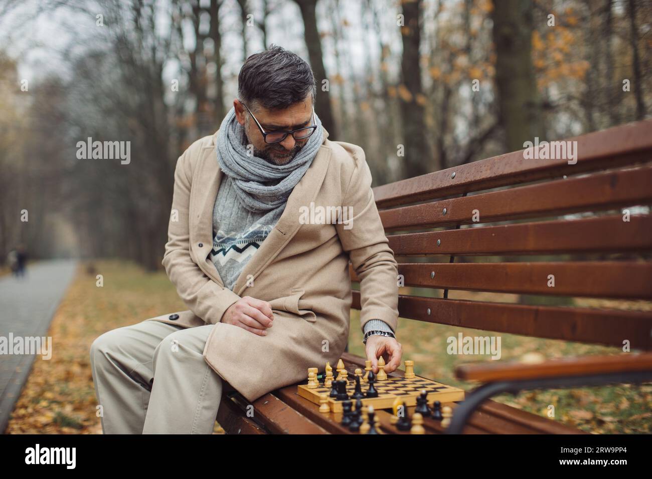 An elderly man plays chess on a bench in an autumn park. Stock Photo