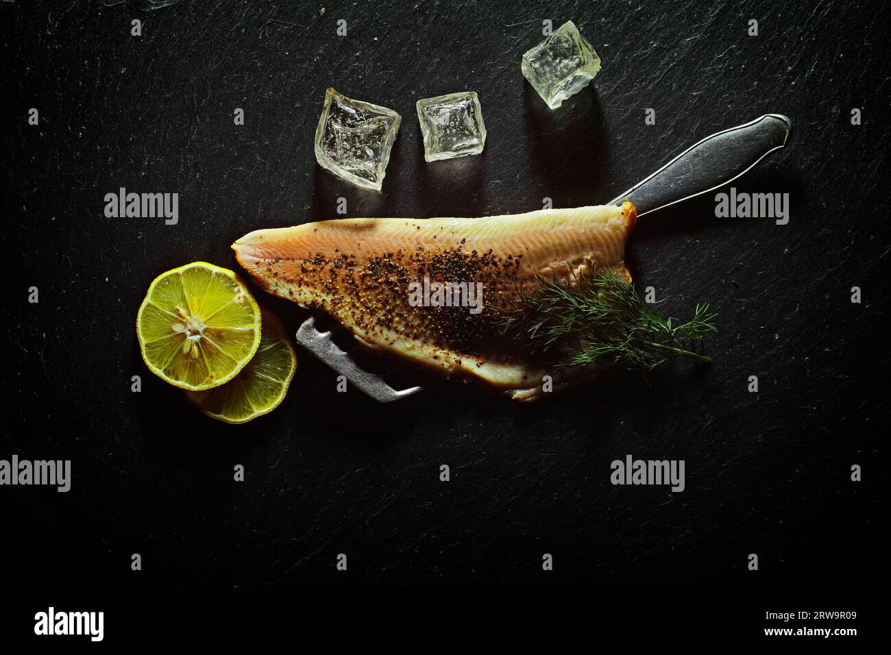 A trout fillet is garnished with lemon, ice cube cubes and dill on a black background Stock Photo