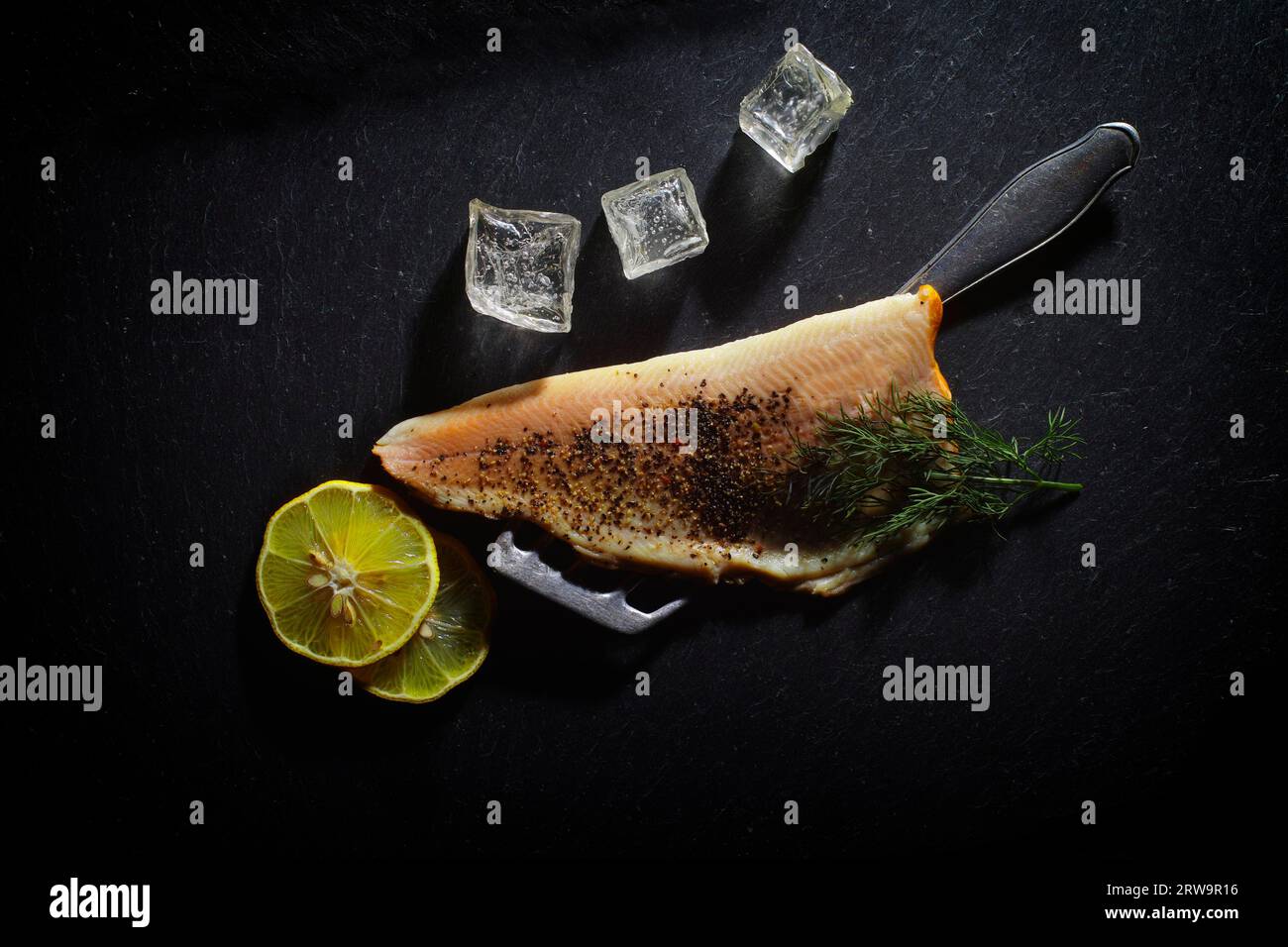 A trout fillet is garnished with lemon, ice cube cubes and dill on a black background Stock Photo