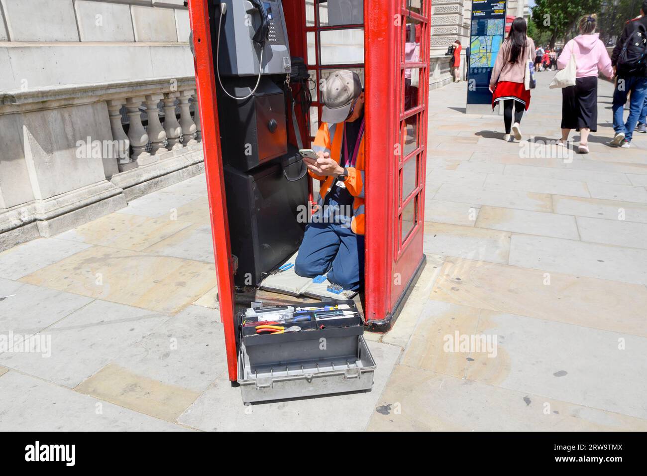 London, England, UK. Repair man on his mobile phone as he repairs a phone box in Parliament Square Stock Photo