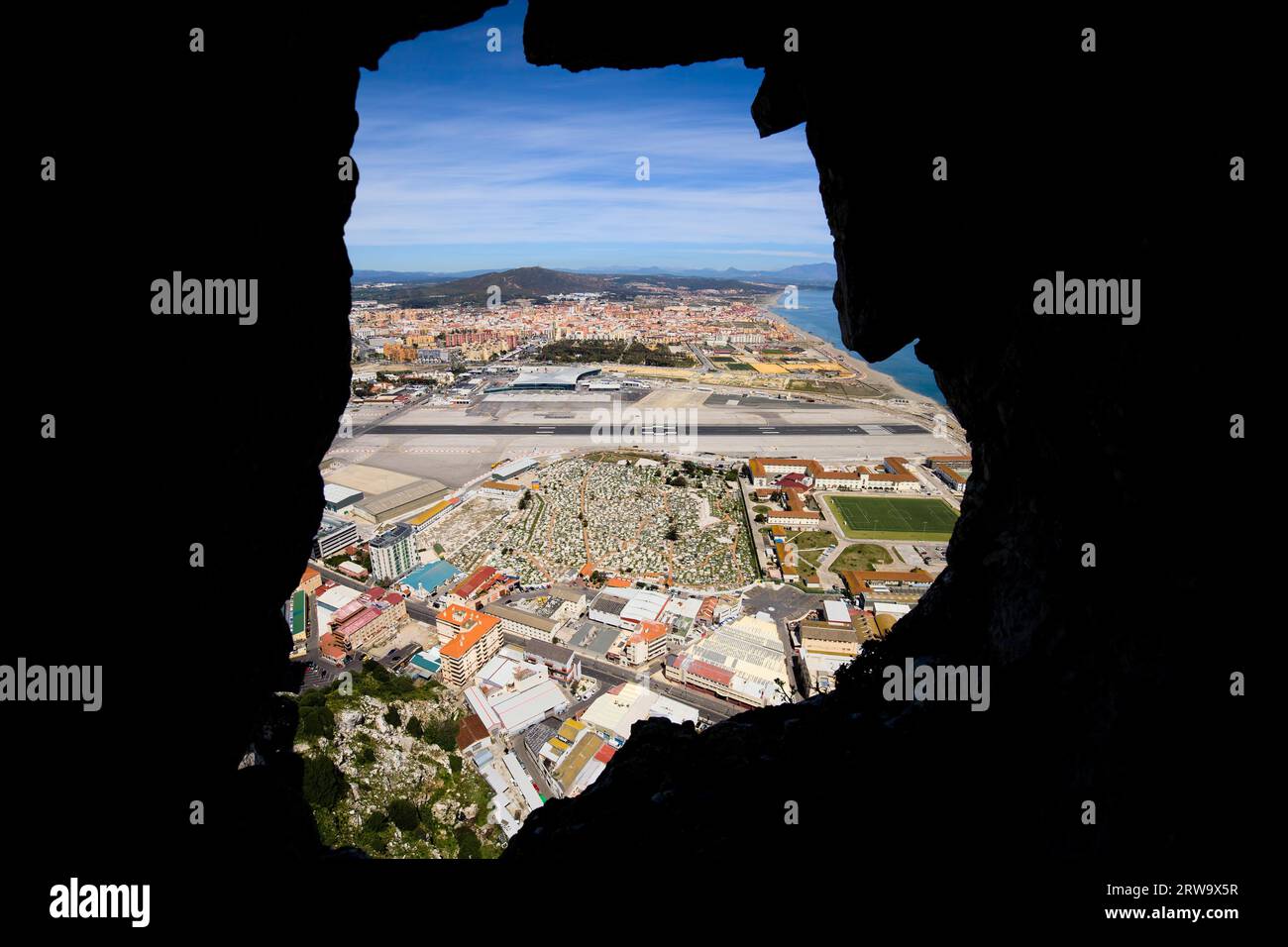 View through a hole in the Gibraltar Rock tunnel on the Gibraltar cemetery, airport runway and La Linea town at the far end Stock Photo