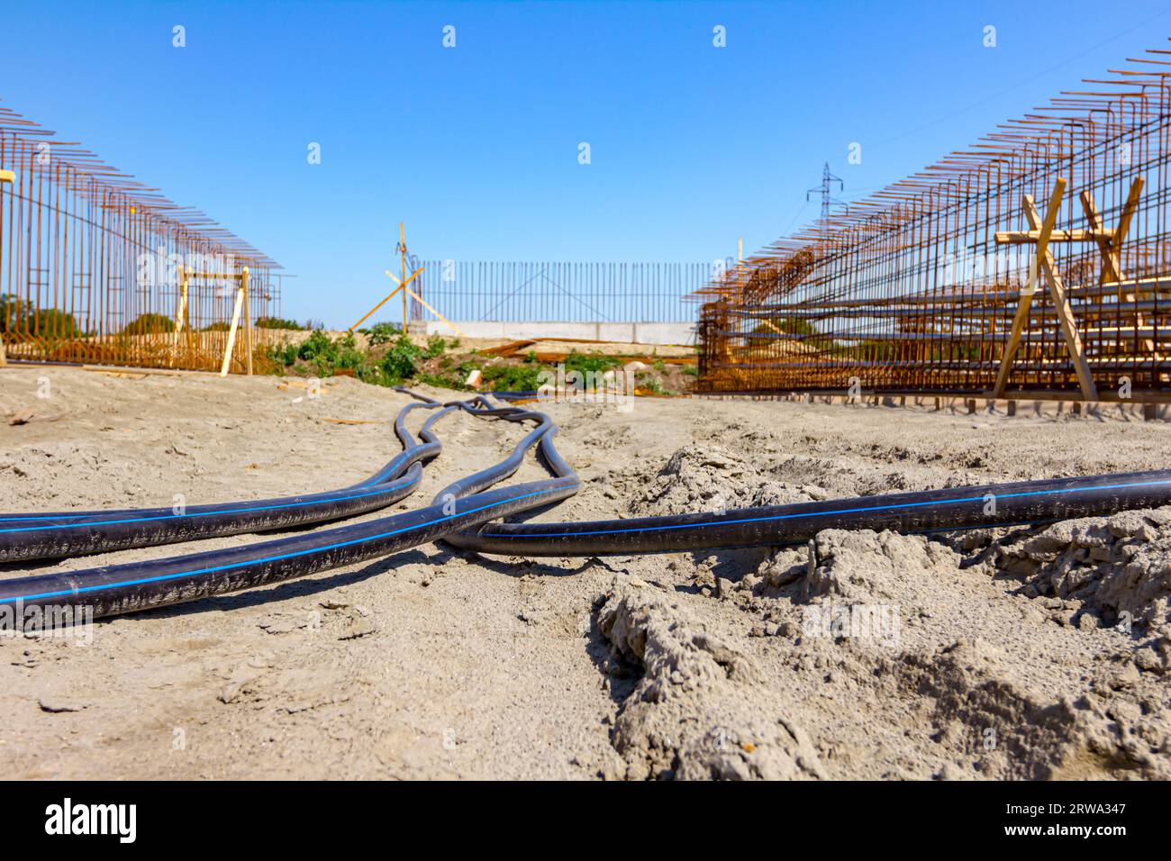 Long black plastic water pipes with blue stripe are placed on ground at