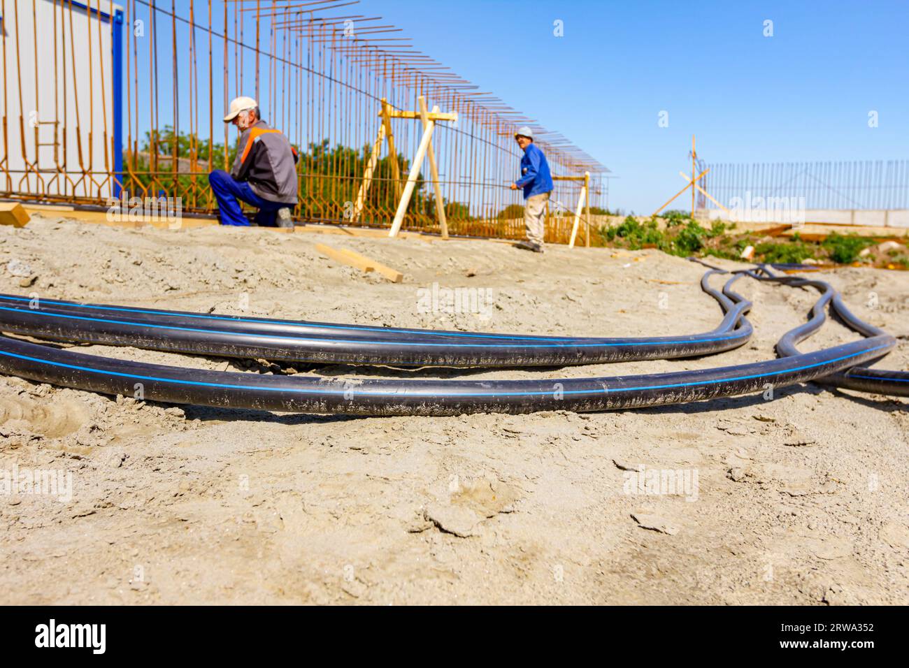 Long black plastic water pipes with blue stripe are placed on ground at