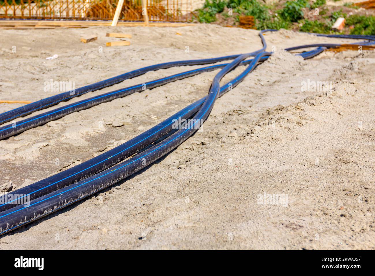 Long black plastic water pipes with blue stripe are placed on ground at
