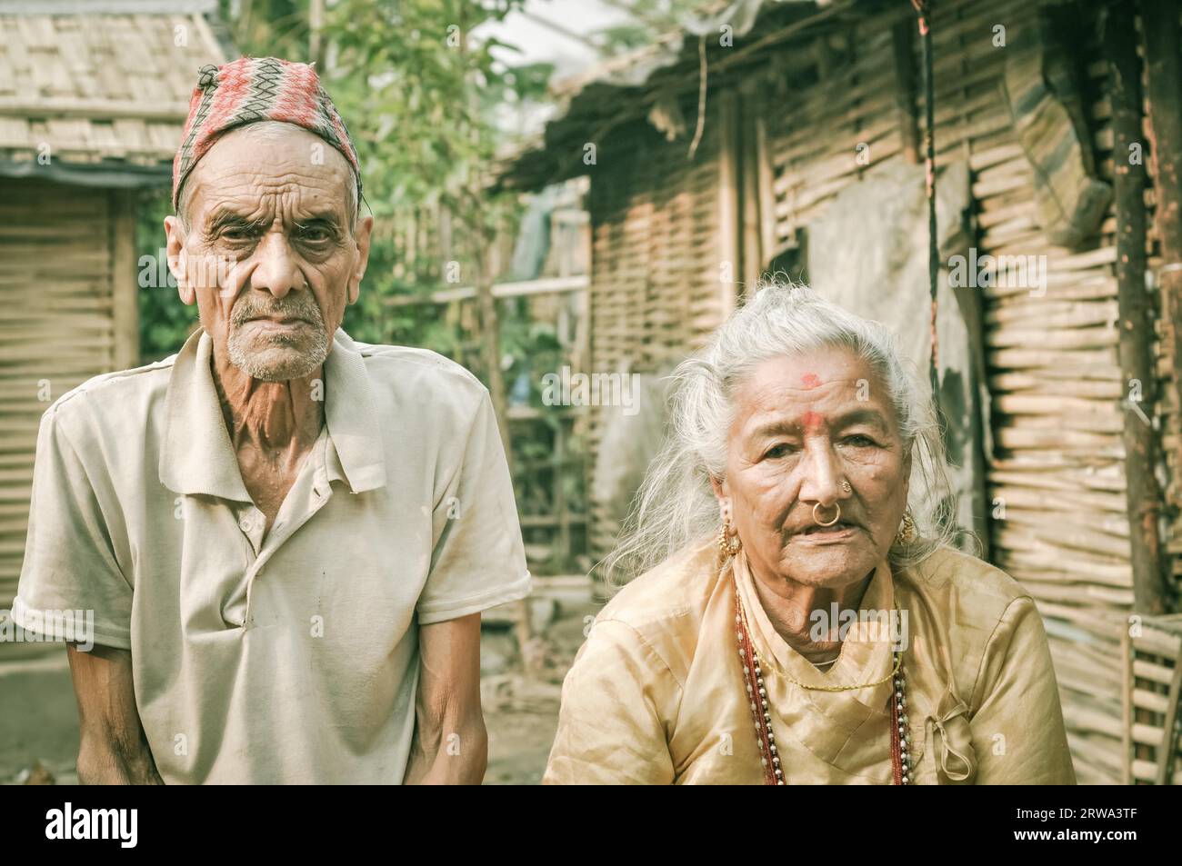 Damak, Nepal, circa May 2012: Old man with wrinkles on his face and with cap on his head frowns and poses with woman at Nepali refugee camp in Damak Stock Photo