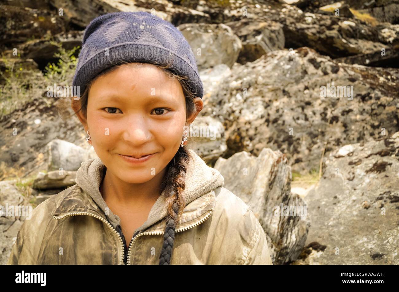 Dolpo, Nepal, circa June 2012: Young brown-haired girl with blue cap and earrings wears brown sweatshirt in beautiful mountains in Dolpo, Nepal. Stock Photo