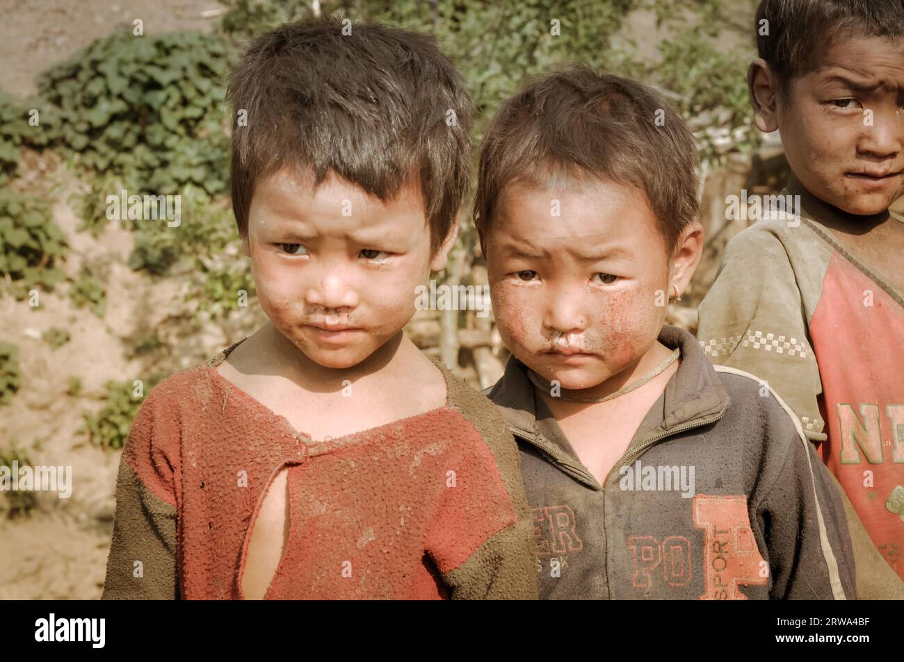 Dolpo, Nepal, circa May 2012: Brown-haired girl and two boys pose and frown to photocamera with dirt on their faces and clothes in Dolpo, Nepal. Stock Photo