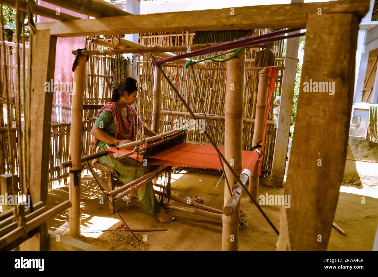 Srimongal, Bangladesh, circa July 2012: Young black-haired woman sits and weaves on simple wooden loom in Srimongal, Bangladesh. Documentary editorial Stock Photo
