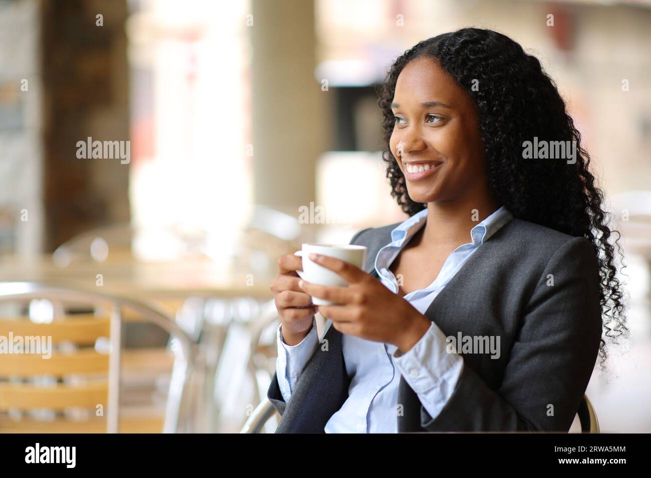 Happy black businesswoman enjoying coffee sitting in a restaurant terrace Stock Photo