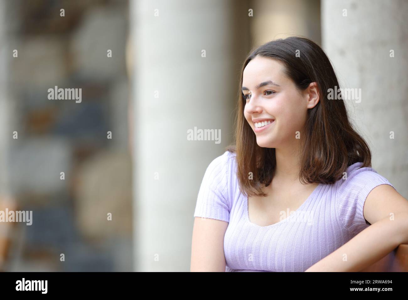 Happy woman sitting in the street looks away Stock Photo